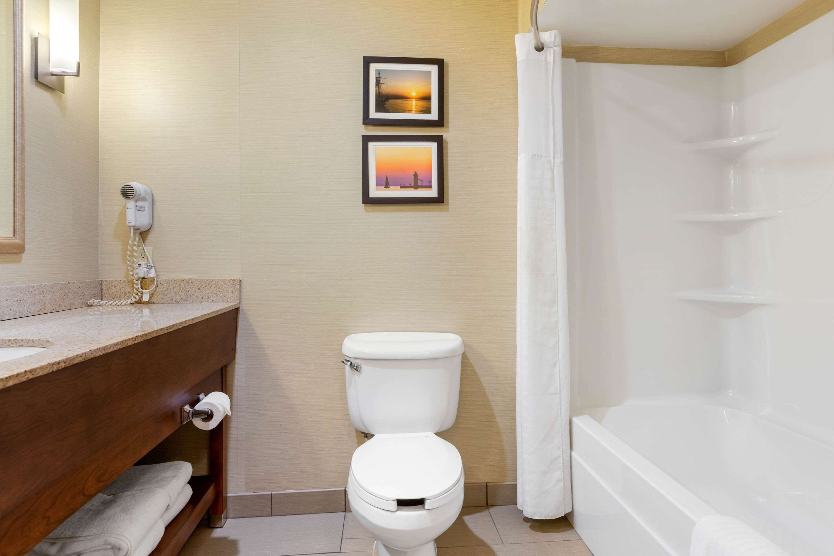 Un baño con inodoro, lavamanos, ducha y dos cuadros en la pared.