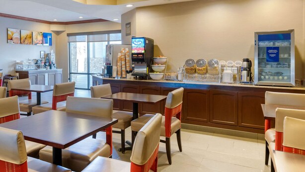 A hotel dining area with tables and chairs, a coffee station, and a view of the outside. - Comfort Suites South Haven near I-96 (South Haven)
