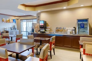 Un comedor de hotel con mesas y sillas, una estación de café y vistas al exterior.