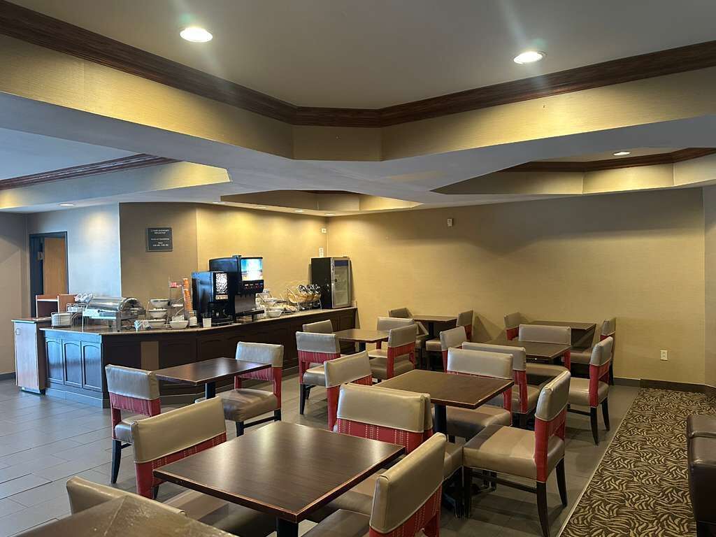 A hotel dining area with multiple tables and chairs, a counter with a coffee machine, and a patterned carpet.