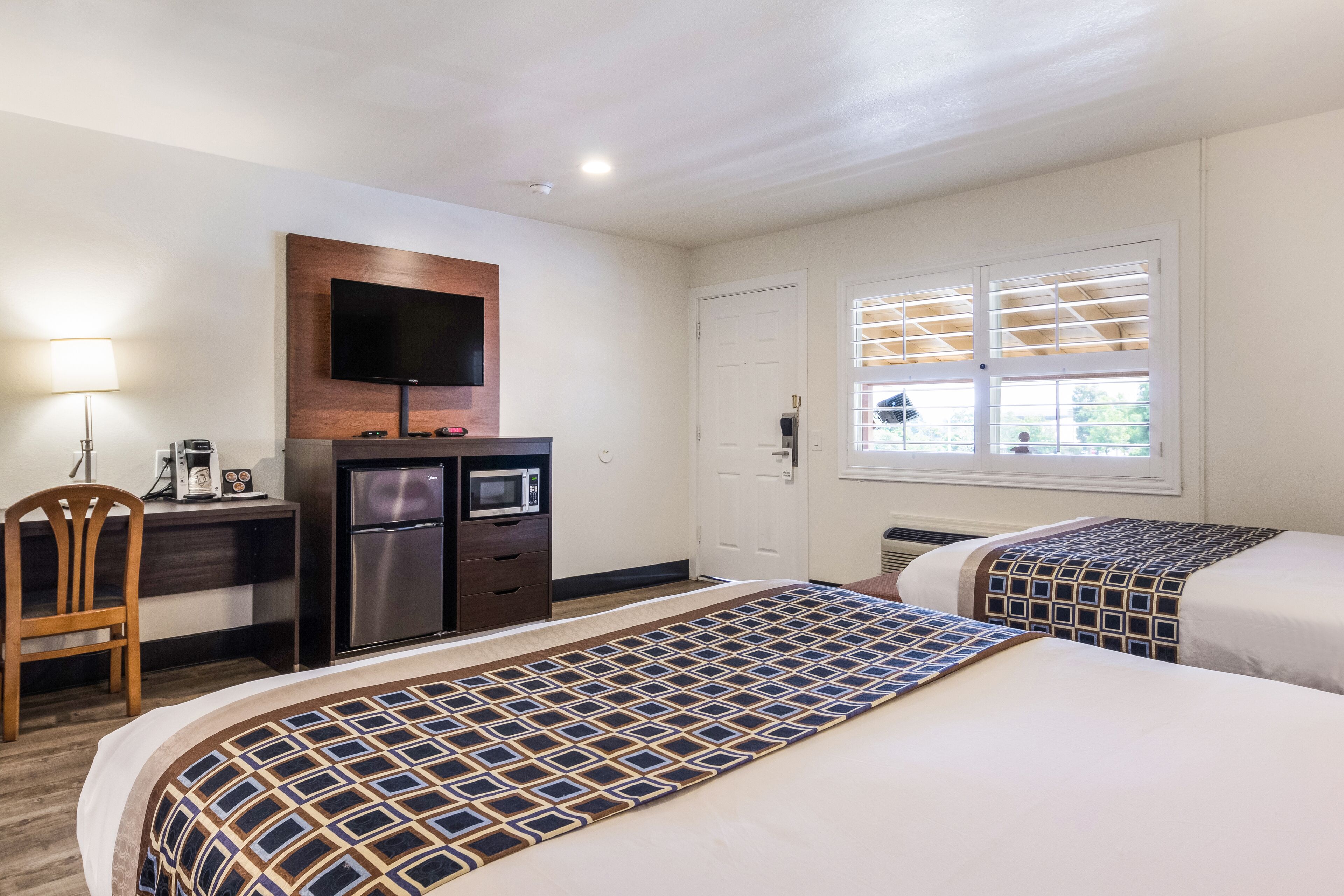 Habitación de hotel con dos camas, un escritorio con televisor, microondas y una silla.