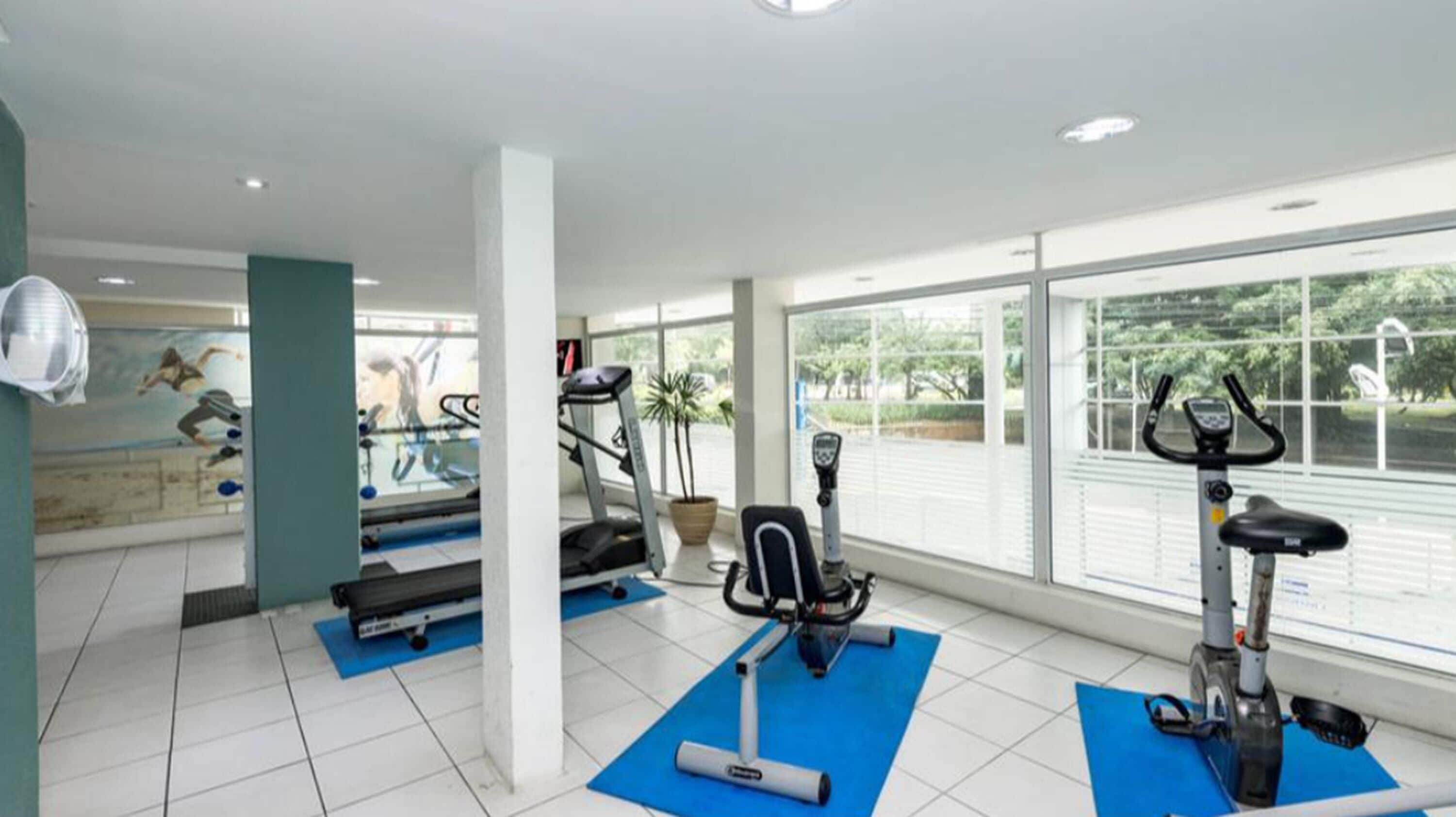 Una palestra con tapis roulant, ellittiche e tappetini per esercizi.