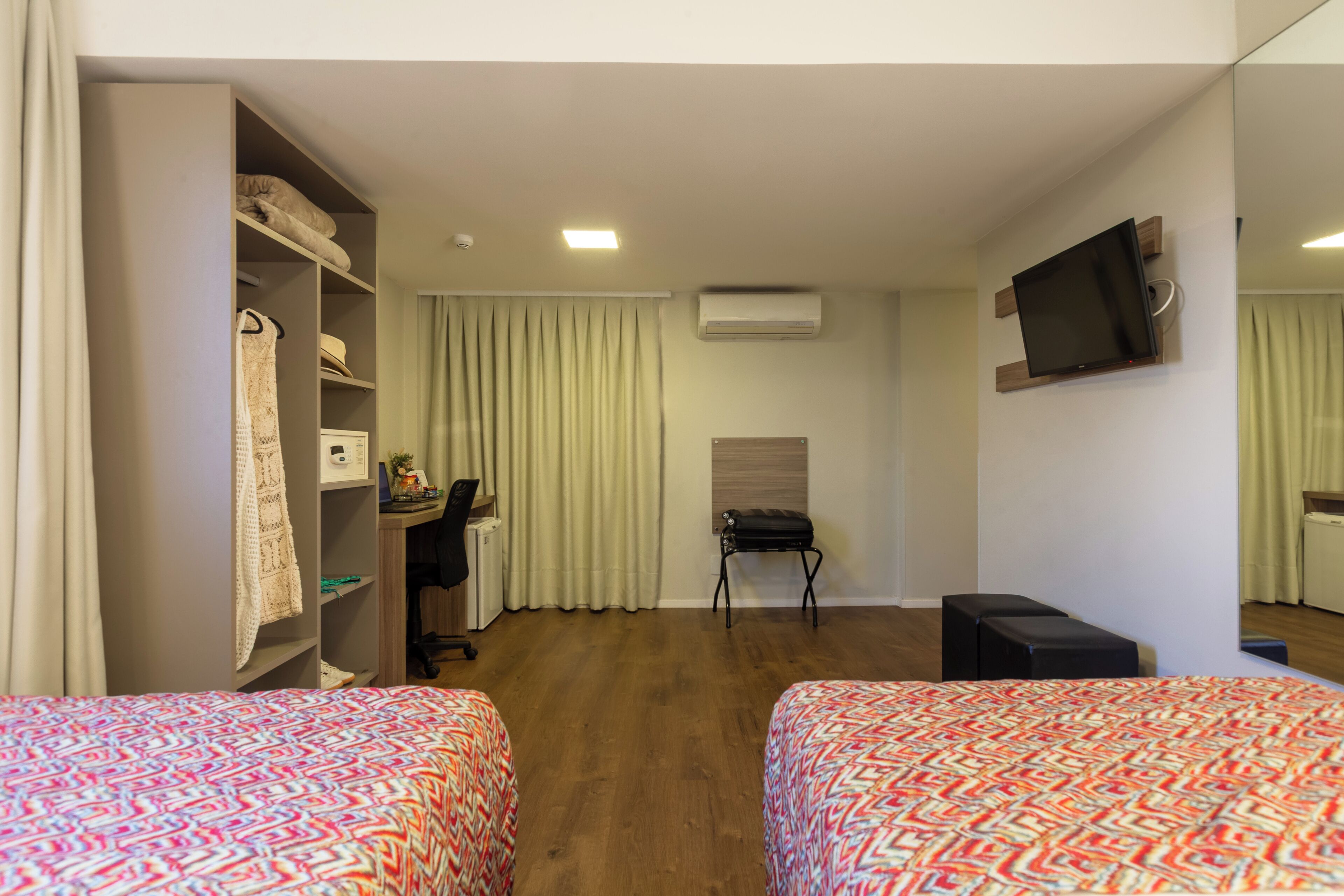 Une chambre d’hôtel avec deux lits, un bureau, une chaise, une télévision et une armoire.