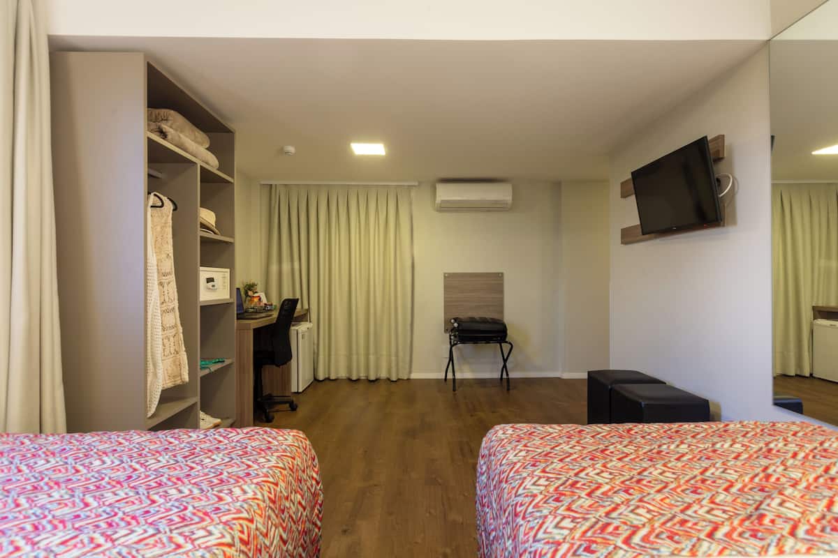 Une chambre d’hôtel avec deux lits, un bureau, une chaise, une télévision et une armoire.