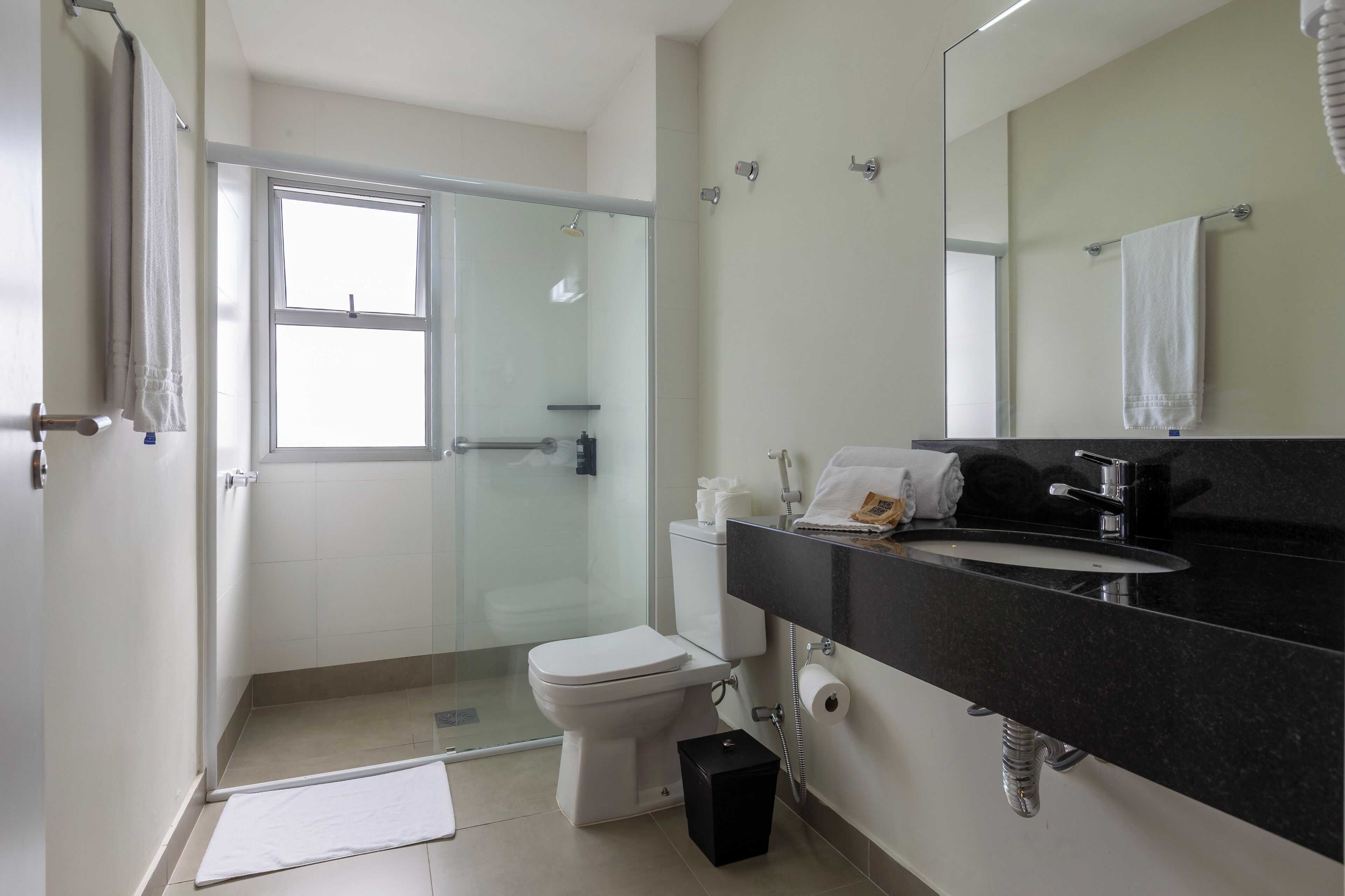 A modern bathroom with a glass shower enclosure, a white toilet, a black sink with a mirror, and a towel rack.