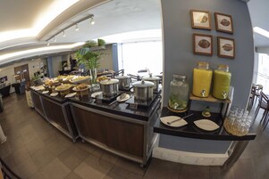 Un buffet garni de divers plats et accompagnements, une plante et des tableaux encadrés accrochés au mur.