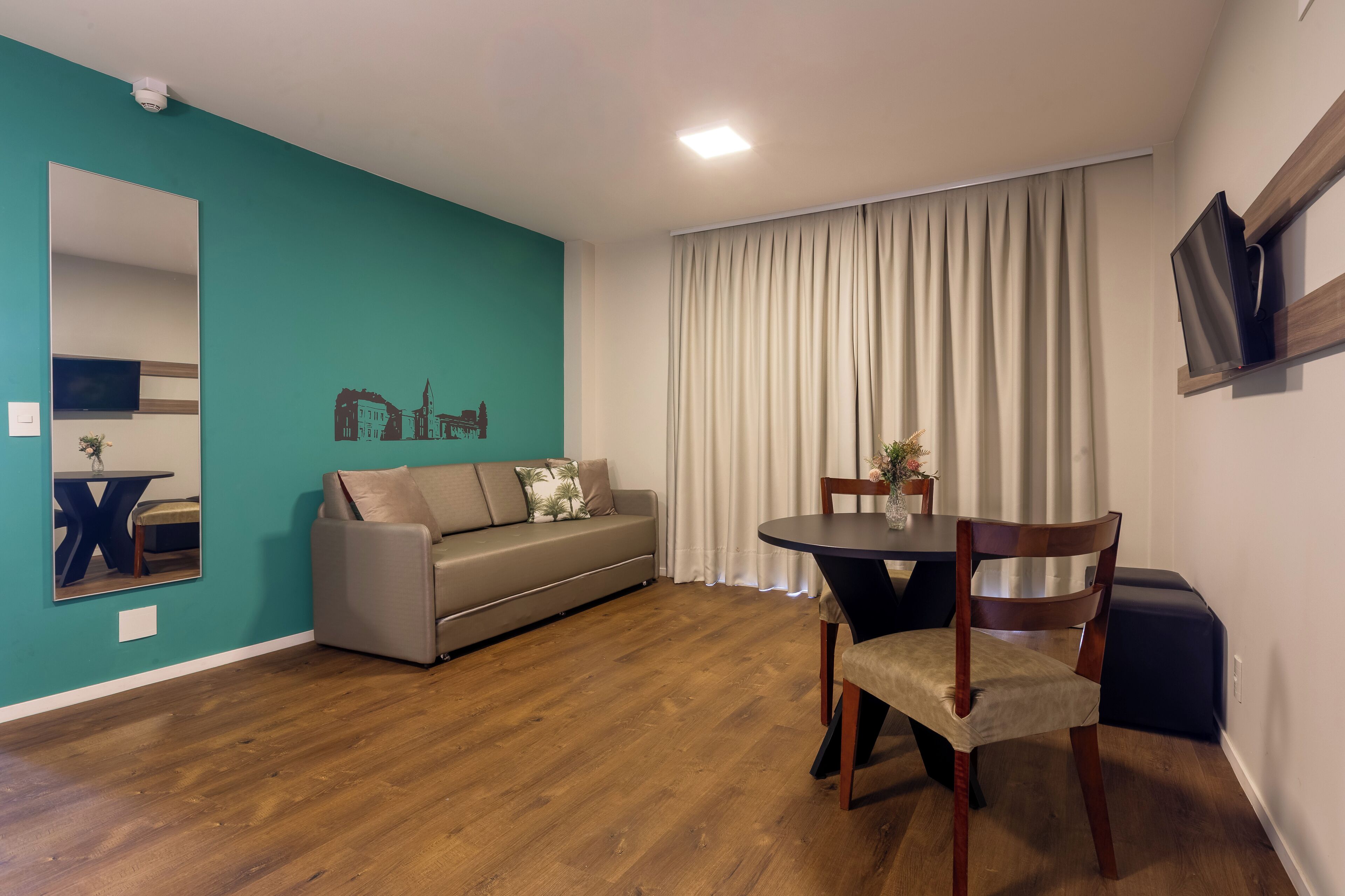 Un salon comprenant un canapé, une table à manger avec des chaises, un miroir et une grande fenêtre avec des rideaux.