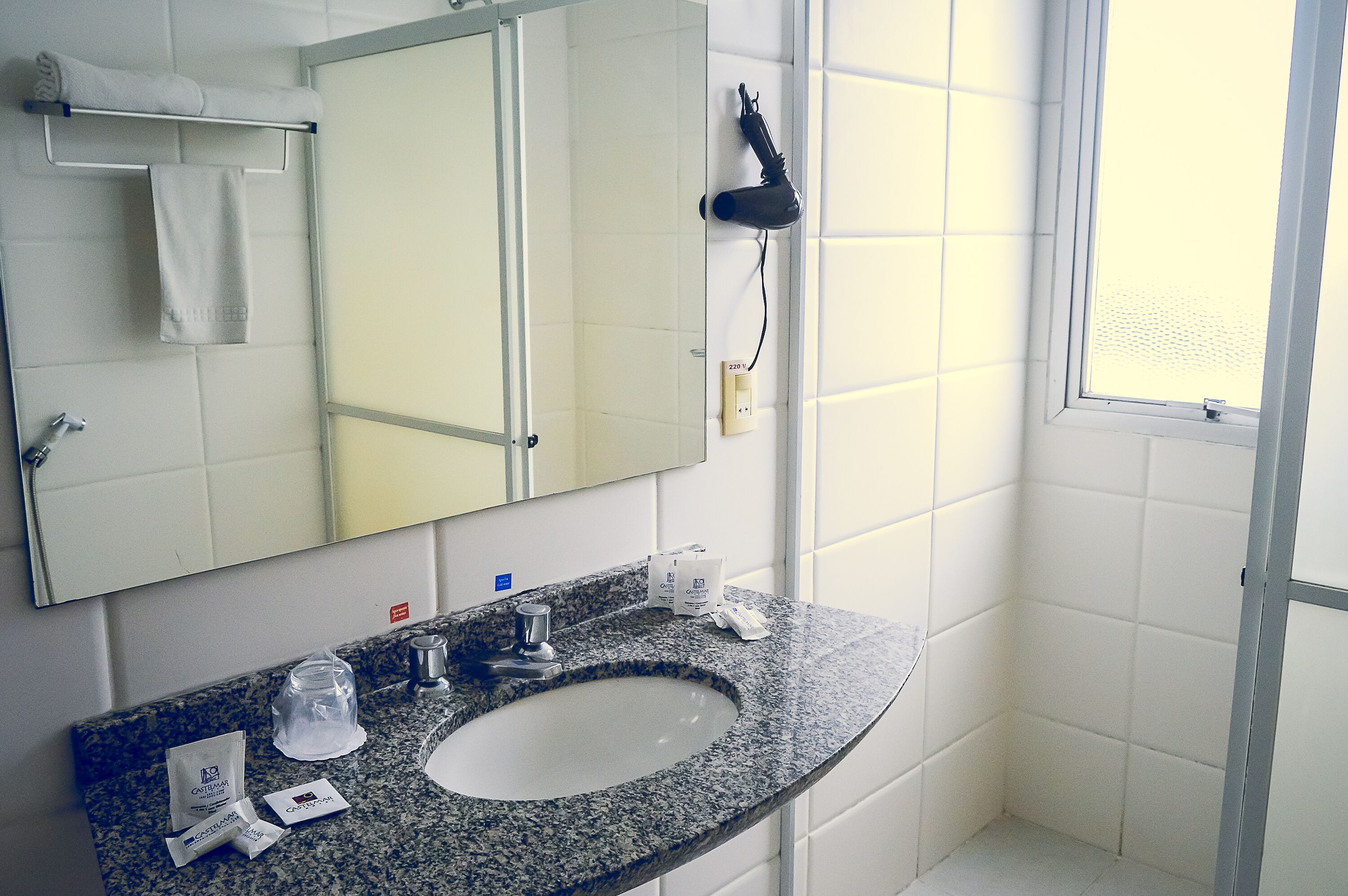 A bathroom with a granite countertop sink, a mirror, a towel rack, and a hairdryer.