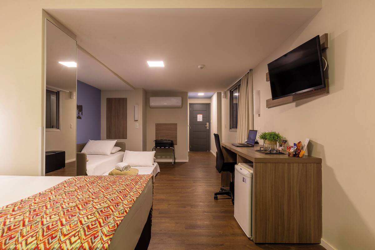 A hotel room with a bed, a desk, a television, and a small kitchenette.