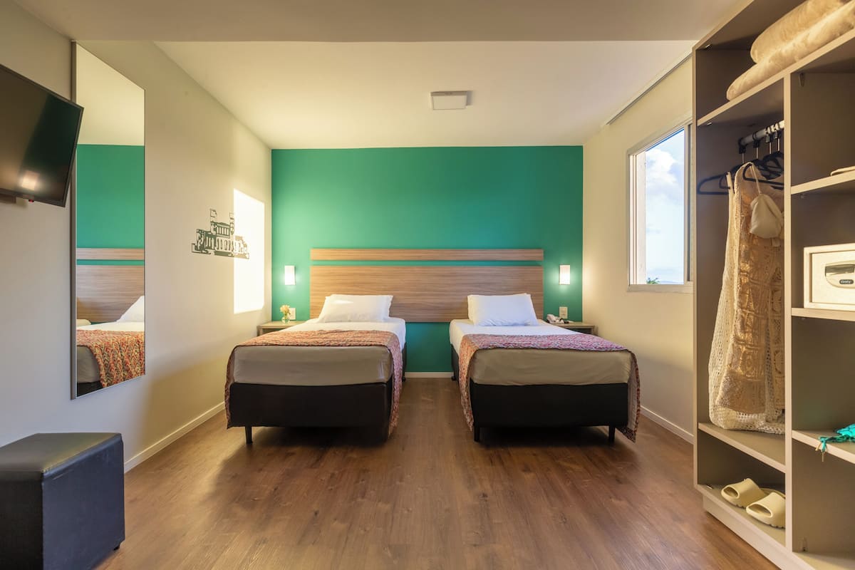 A hotel room with two beds, a large mirror, a wardrobe, and a window.