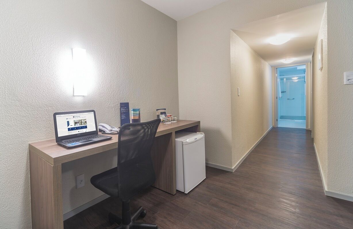 A compact office space with a desk, chair, laptop, and a small refrigerator.