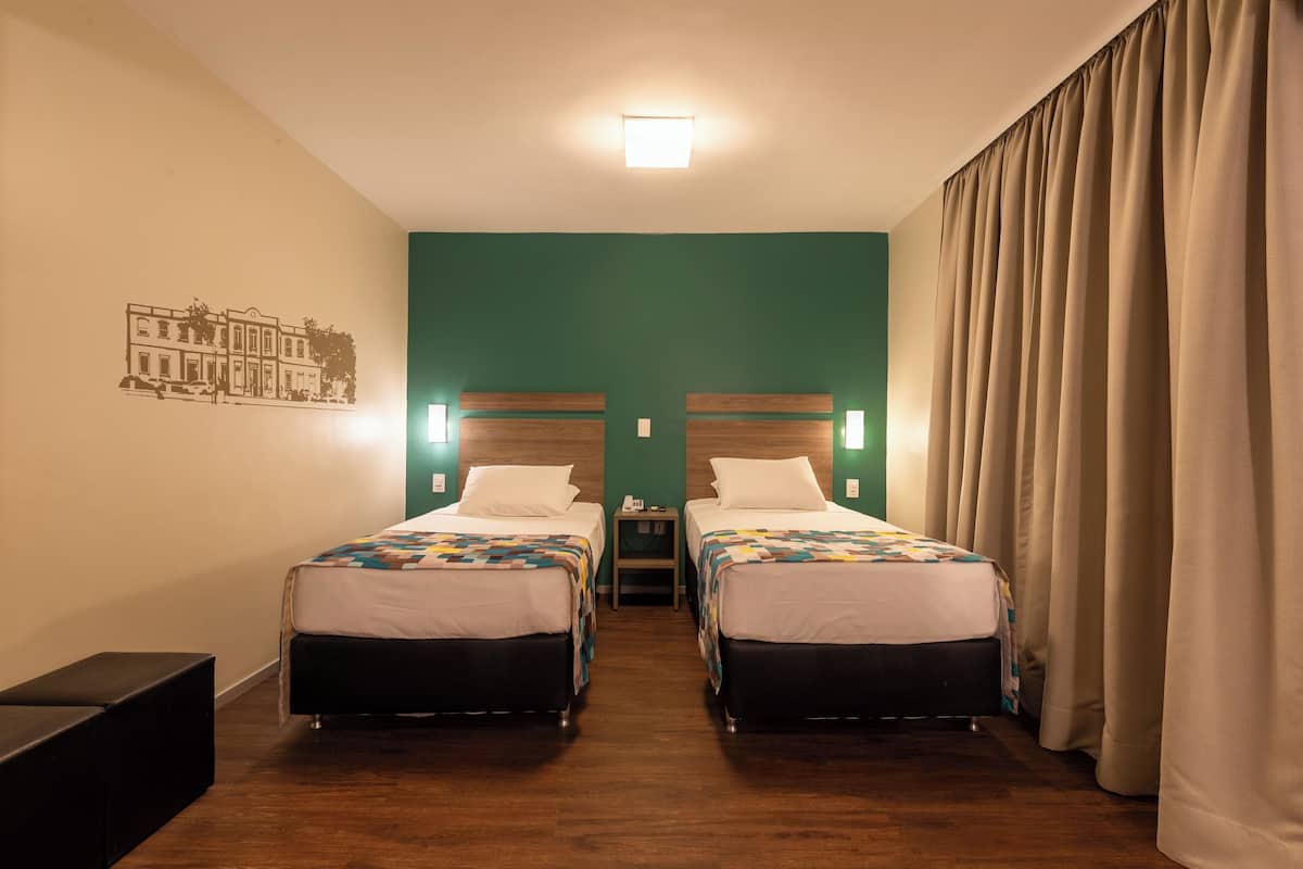 Une chambre d’hôtel avec deux lits, une table de chevet, une décoration murale représentant un bâtiment et un rideau.