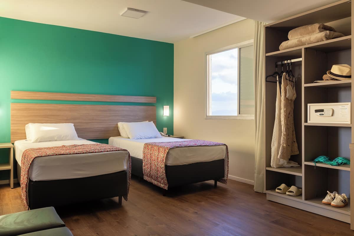 Une chambre d’hôtel avec deux lits, une armoire et une fenêtre.