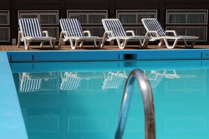 Area piscina con quattro sdraio a righe e una scala in metallo.