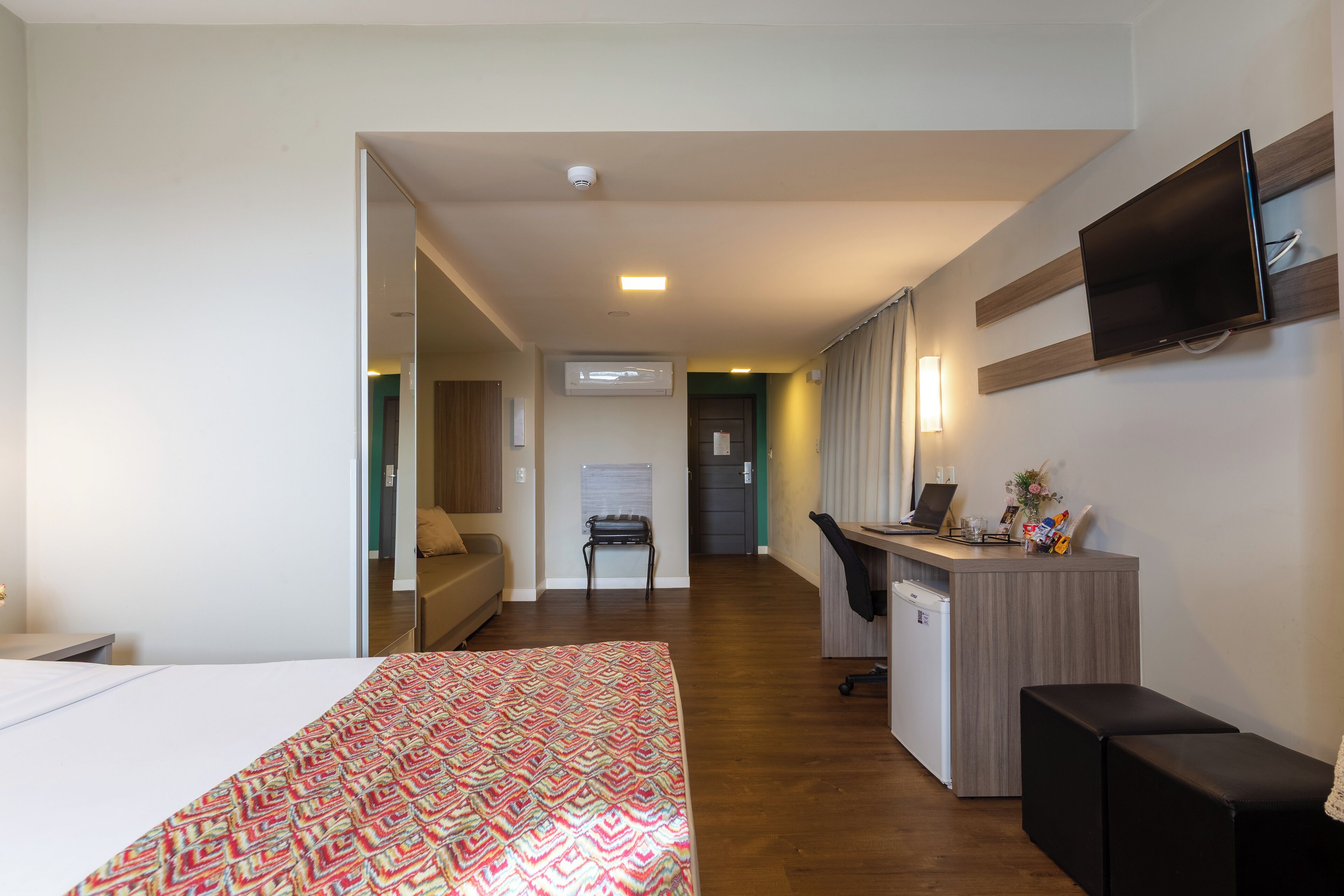 A hotel room with a bed, a desk, a TV, and a kitchenette.