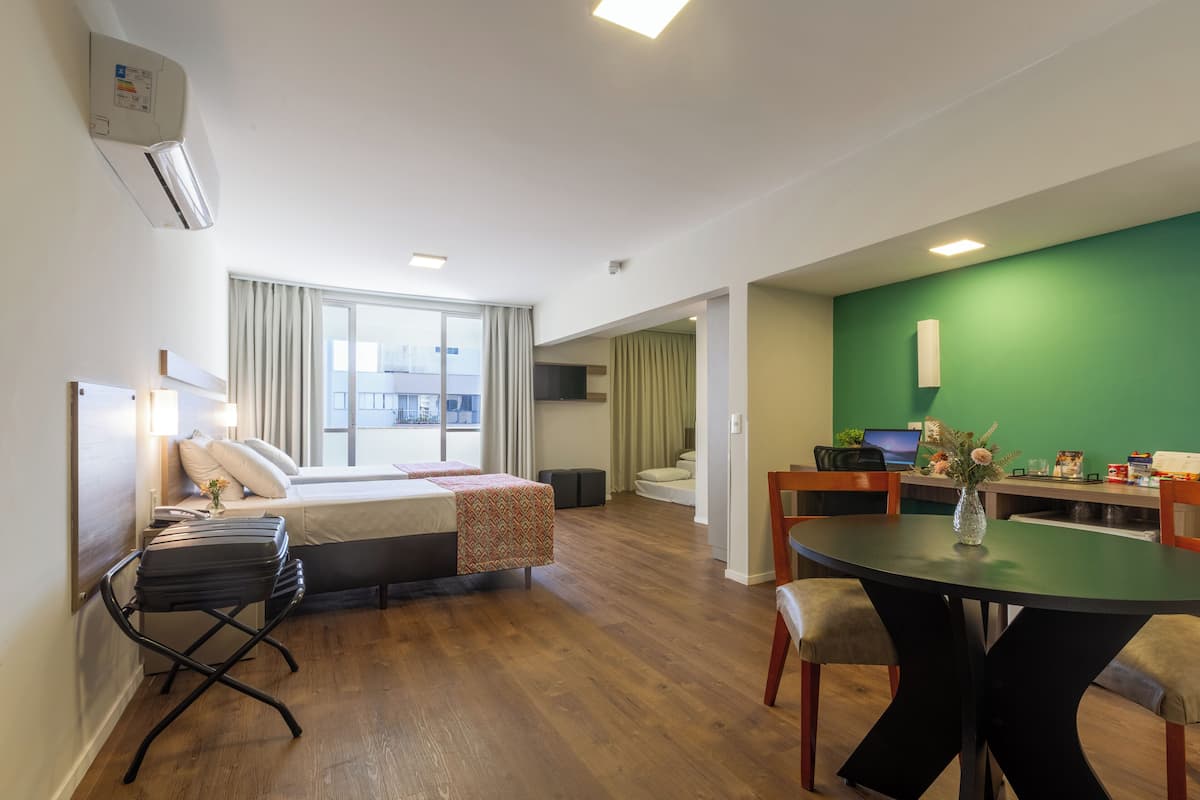 A modern hotel room with a bed, bedside tables, a desk, and a dining area.