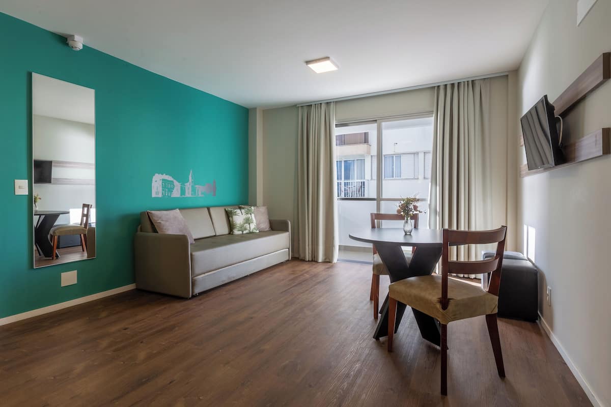 Un salon moderne avec un mur d’accent de couleur turquoise, un canapé gris, une table à manger avec des chaises et une grande fenêtre avec des rideaux.