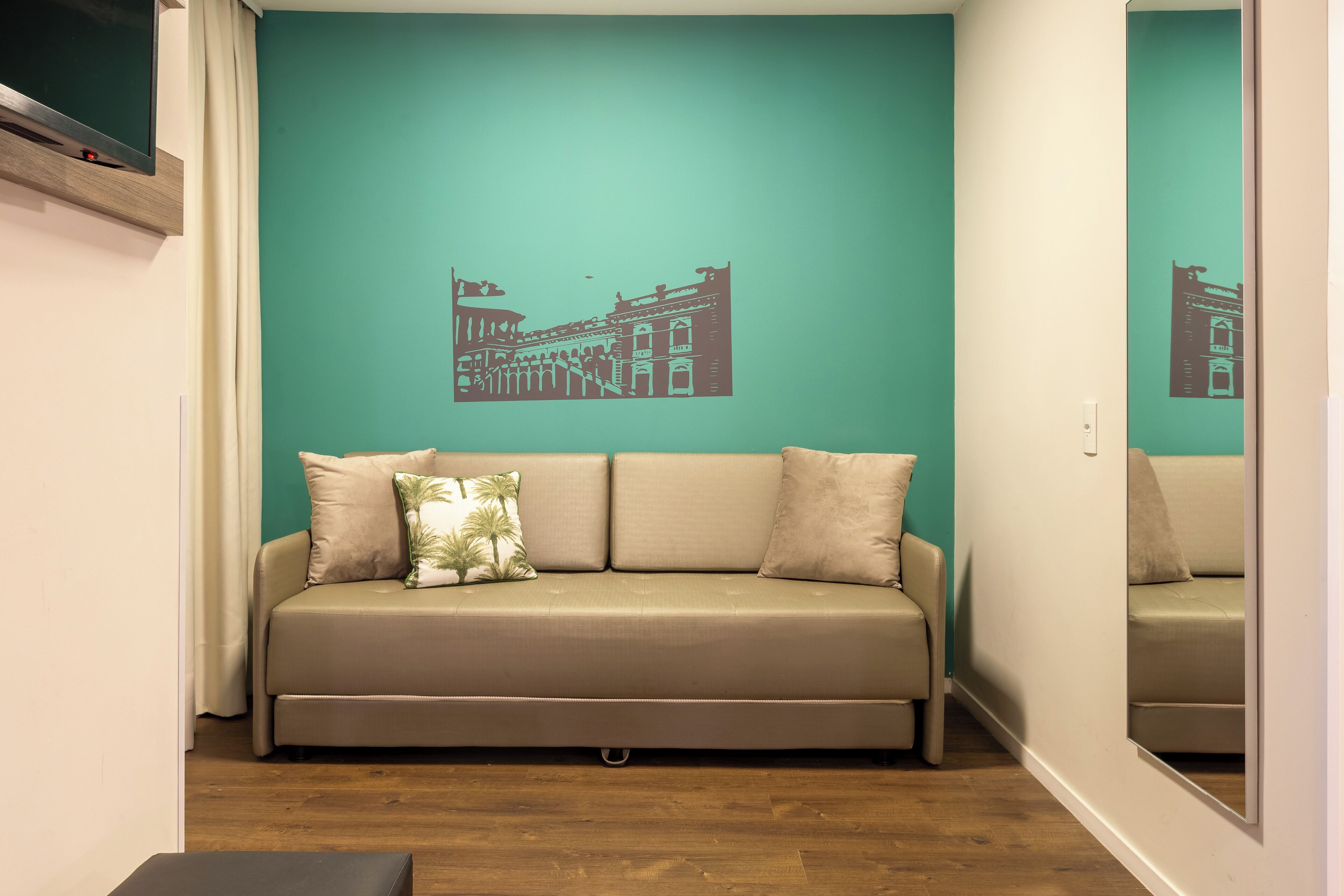 A room with a teal-colored wall, a beige sofa with cushions, and a wooden floor.