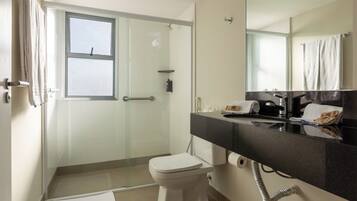 Une salle de bain moderne avec une douche à l’italienne en verre, des toilettes blanches, un meuble-lavabo noir et un grand miroir.