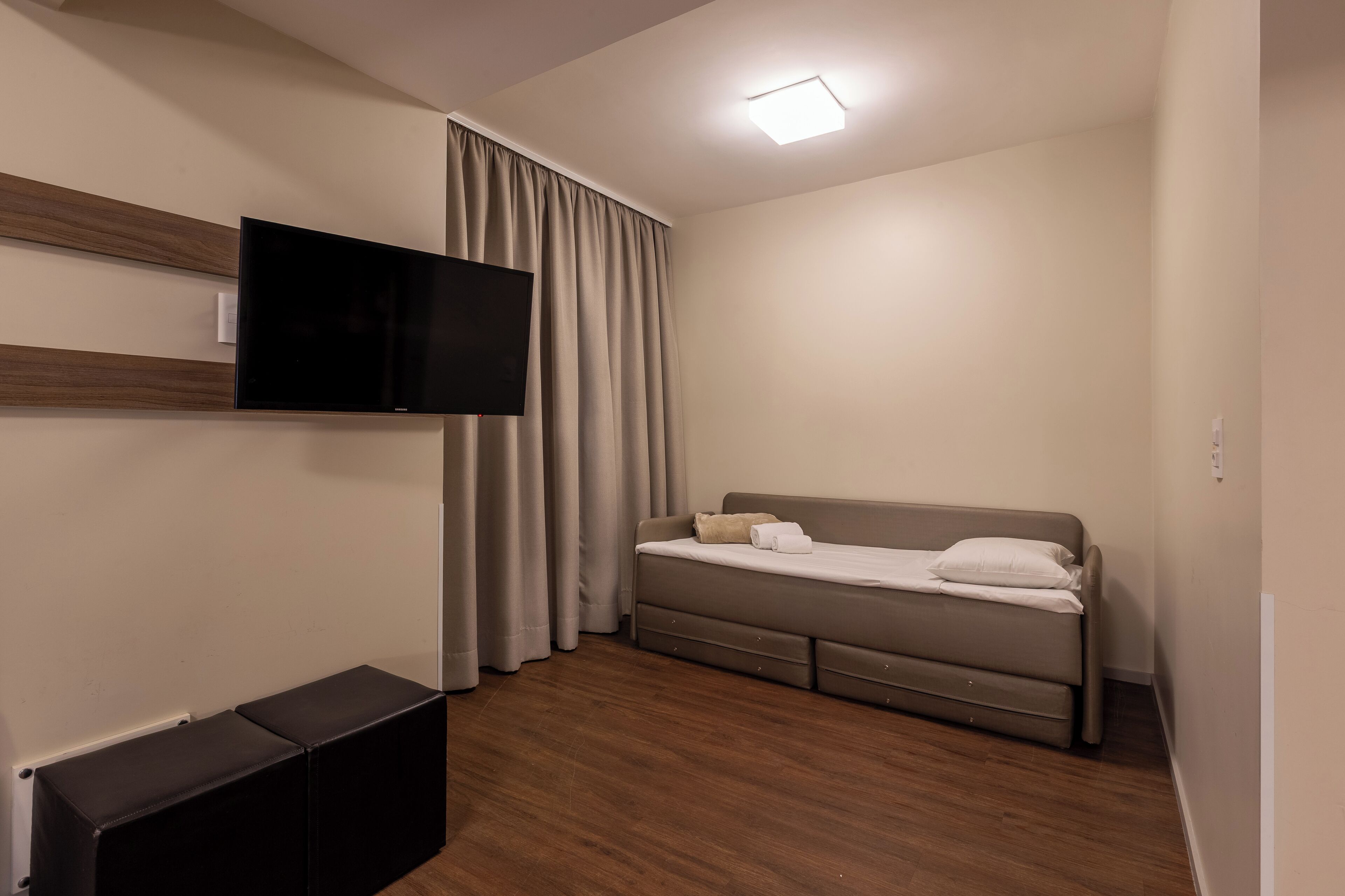 Une chambre moderne avec un téléviseur à écran plat fixé au mur, un lit avec une tête de lit et un luminaire au plafond.