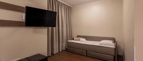 Une chambre moderne avec un téléviseur à écran plat fixé au mur, un lit avec une tête de lit et un luminaire au plafond.