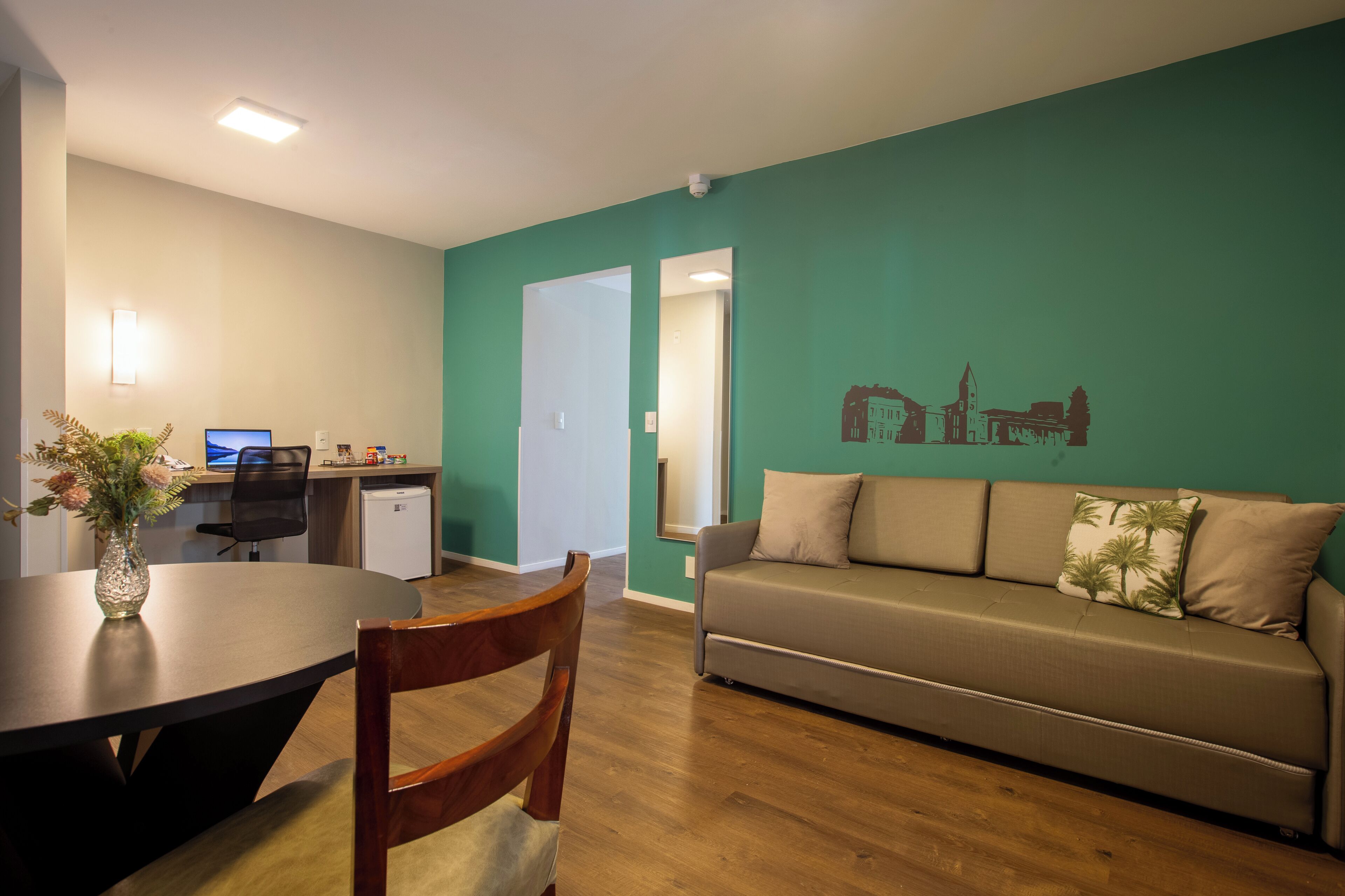 A living room with a sofa, a dining table with chairs, a small kitchen area, and a wall with a mural.