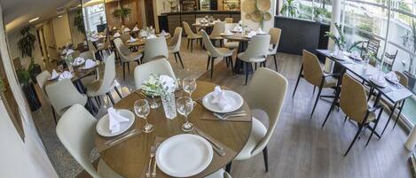 Un restaurante con mesas redondas, sillas blancas y una zona de bar.