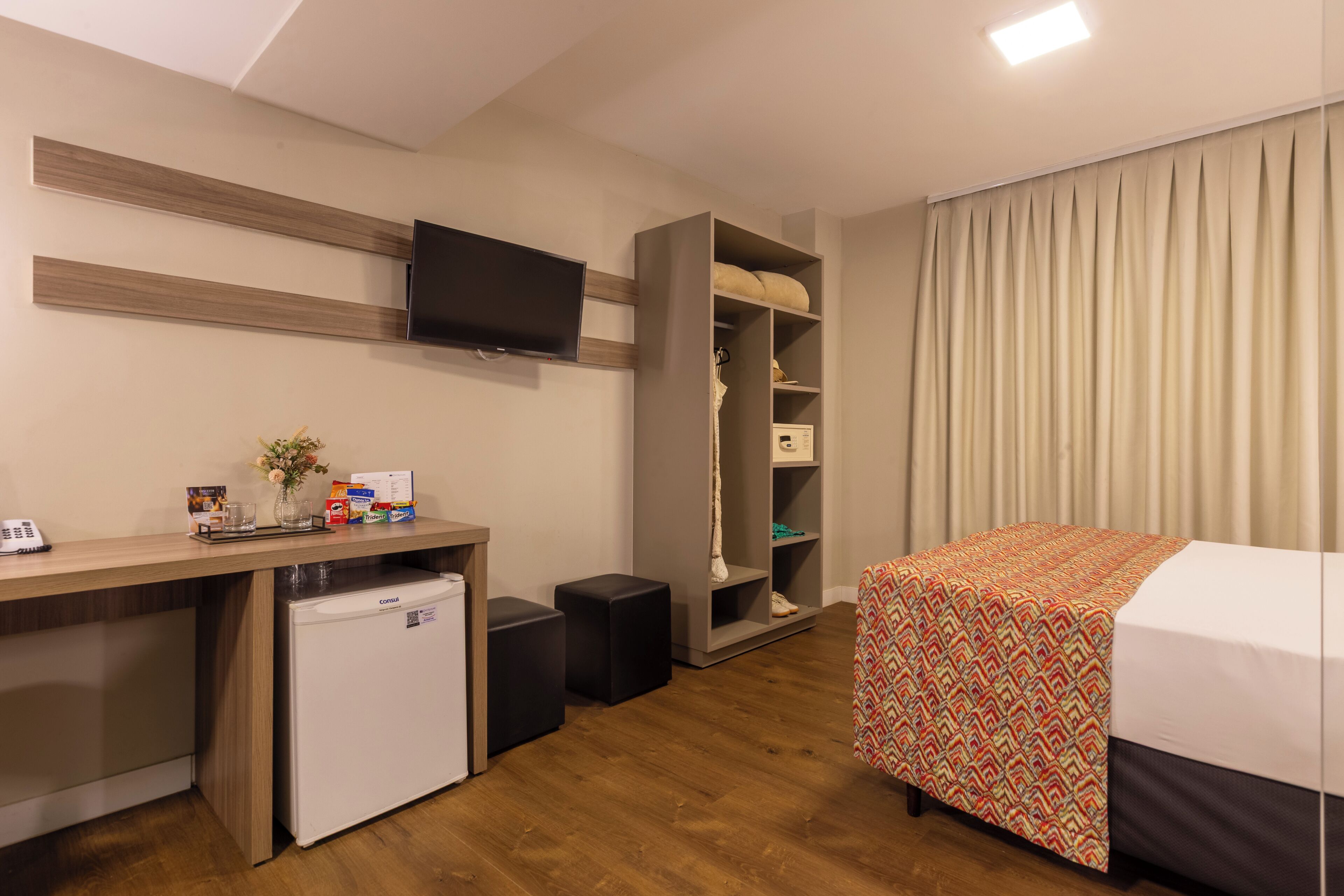 A hotel room with a bed, a desk with a refrigerator, a television, and a wardrobe.