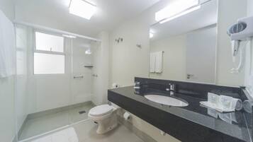 A modern bathroom with a glass shower enclosure, a white toilet, a black countertop with a sink, and a hairdryer mounted on the wall.