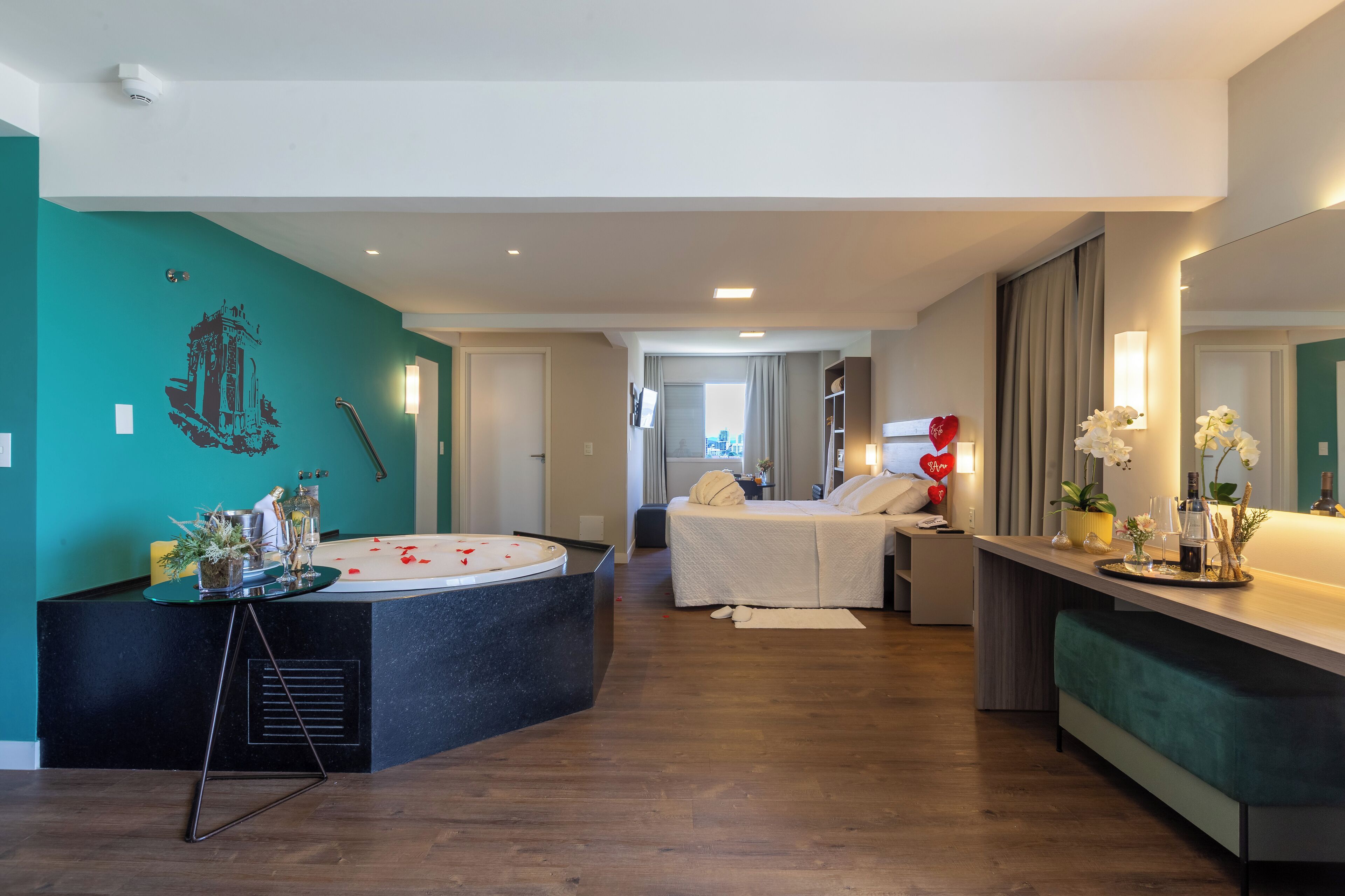 A modern hotel room with a spa area, a bed, a sitting area with a view, and a reception desk.
