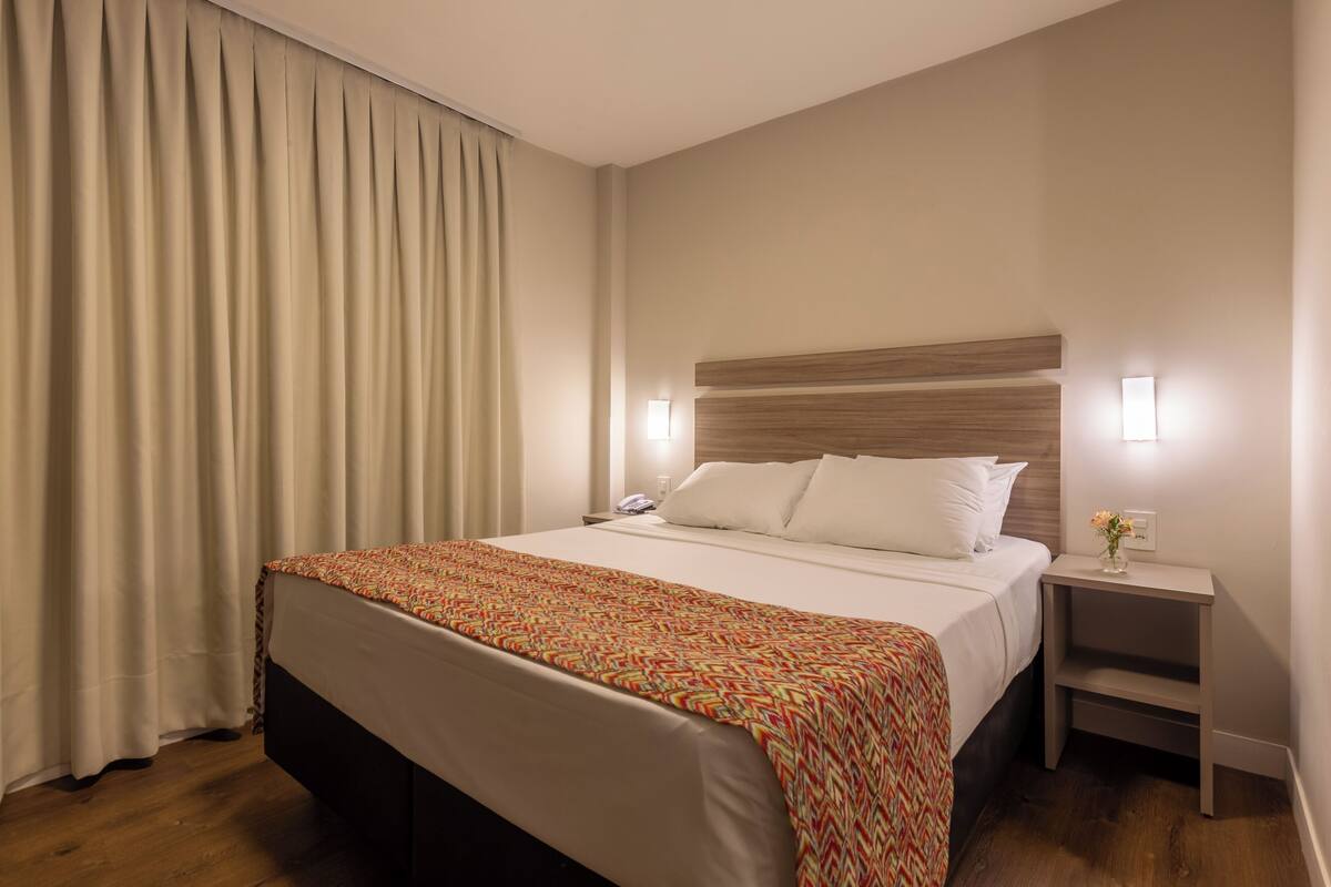 Une chambre d’hôtel avec un grand lit, une table de chevet avec une lampe et une fenêtre avec des rideaux.