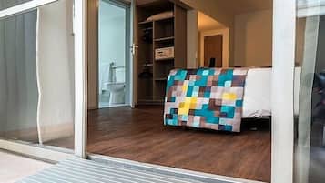 Una habitación con cama, suelo de madera, puerta corrediza de vidrio, armario y una mesita pequeña.