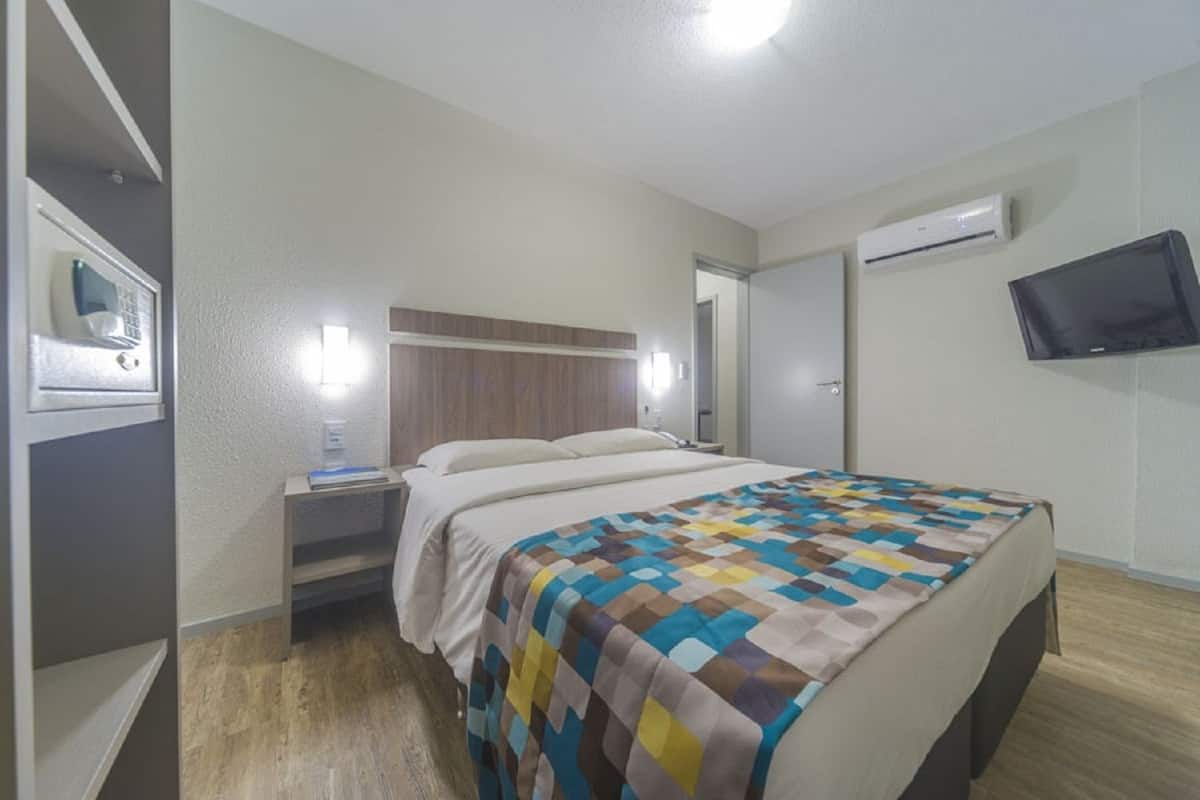 A hotel room with a bed, bedside table, nightstand, and a flat-screen TV mounted on the wall.
