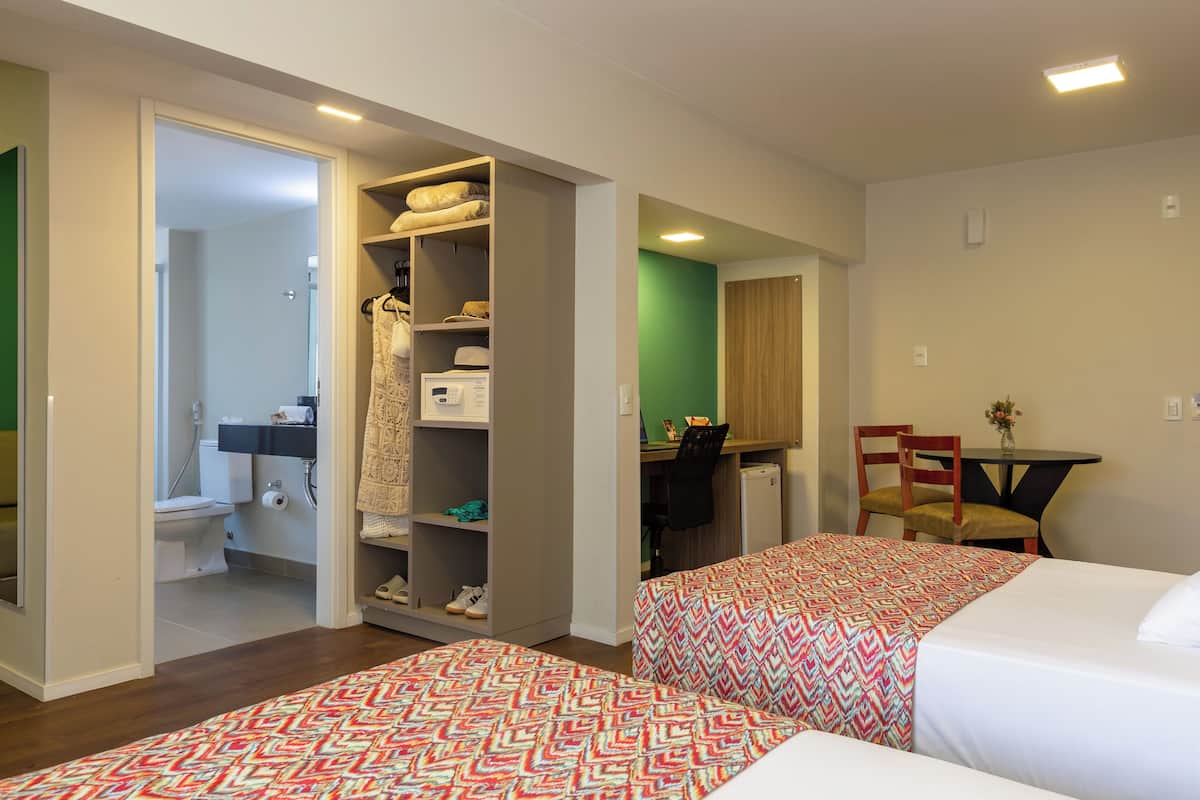 Une chambre d’hôtel avec deux lits, un bureau, une chaise, une petite table, une armoire et une salle de bain.