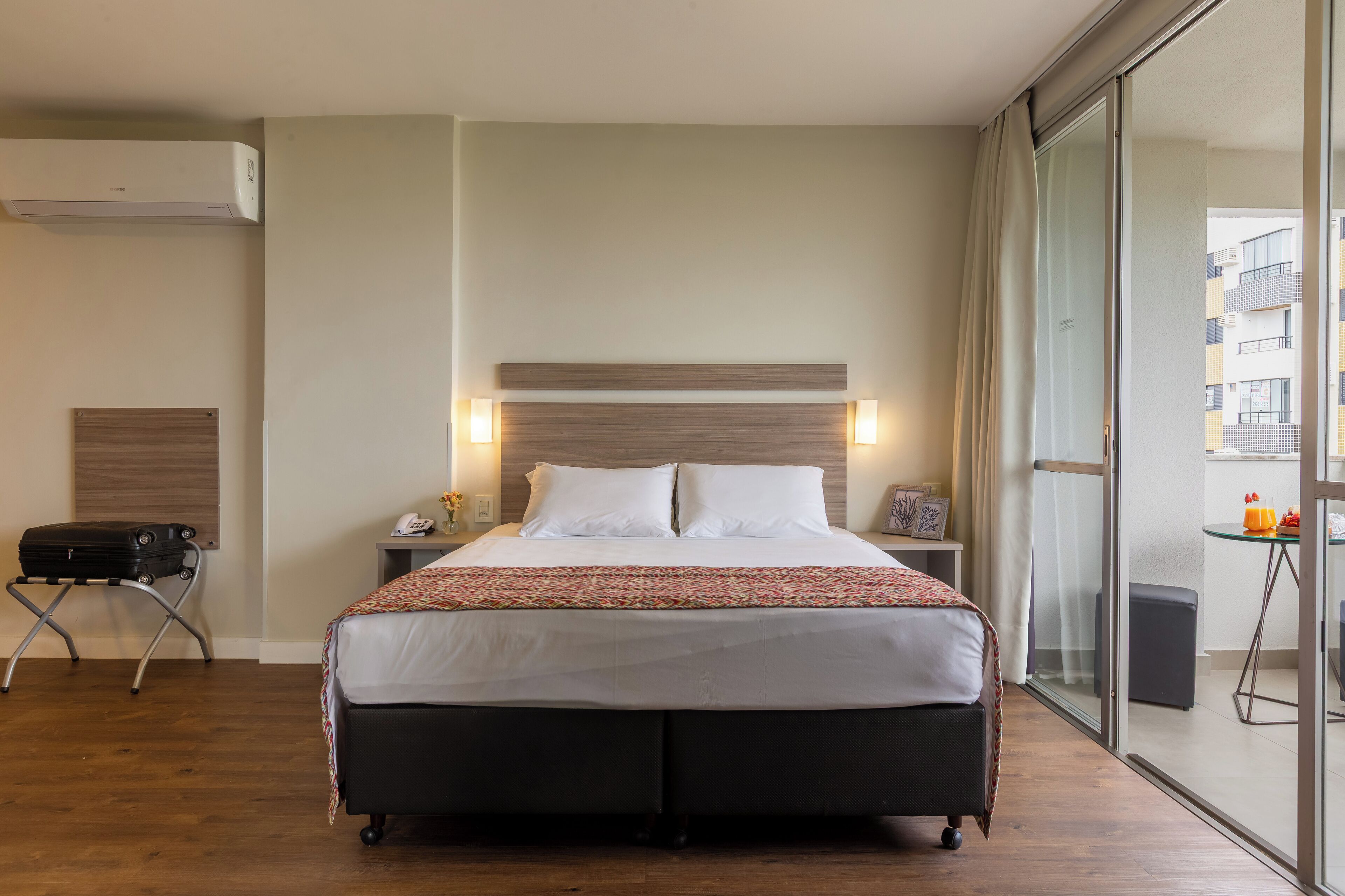 A hotel room with a large bed, bedside lamps, a suitcase, and a view of the outside.