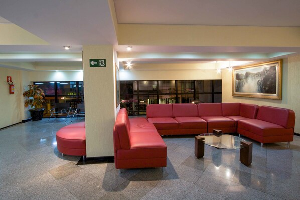 Un vestíbulo moderno con un sofá seccional rojo, una mesa de centro de vidrio y un cuadro grande en la pared.