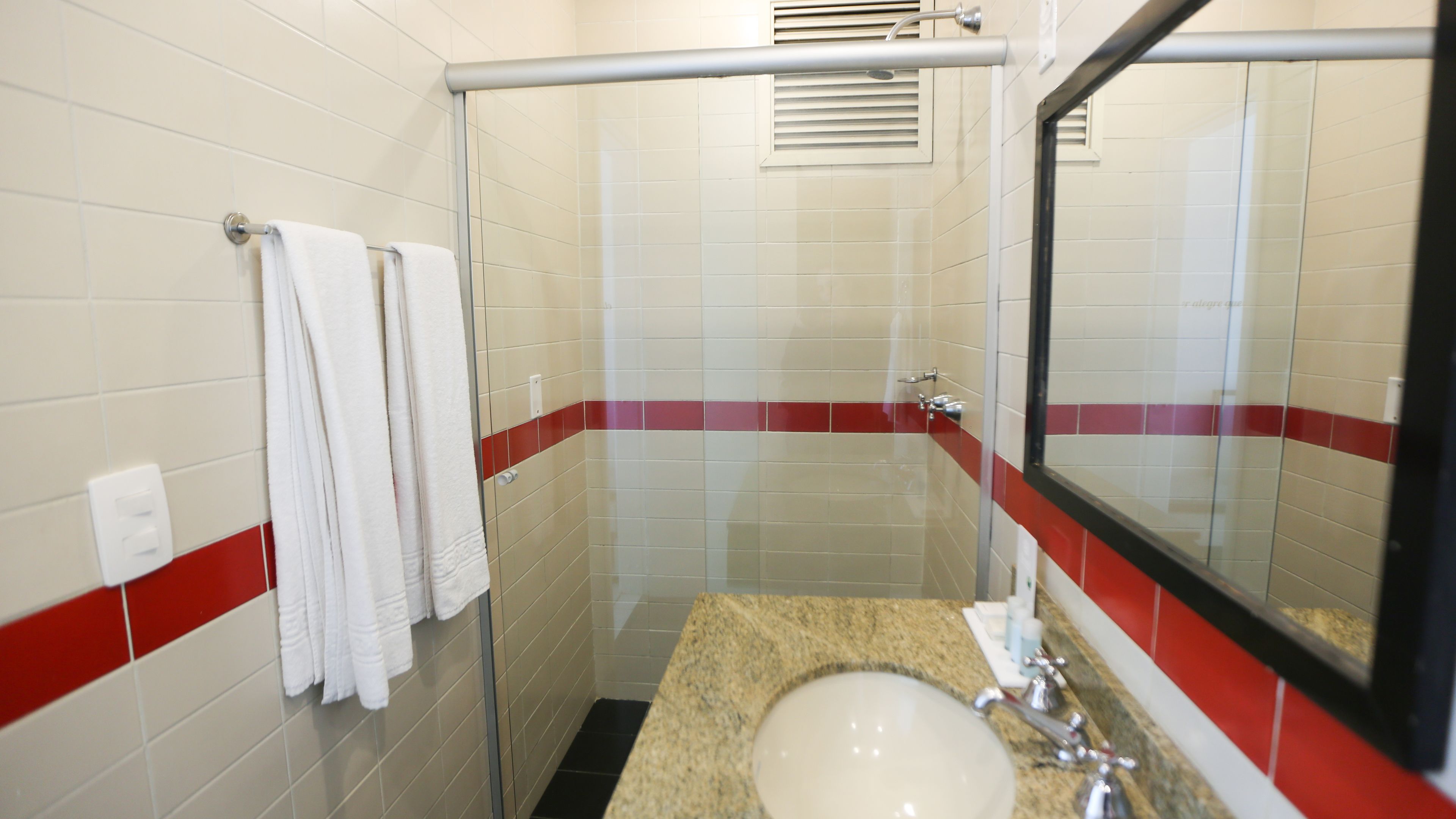 A bathroom with a glass shower enclosure, a sink with a granite countertop, and a mirror with a red stripe.