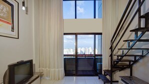 A modern living room with a television, a bench, and a staircase leading to a balcony with a city view.