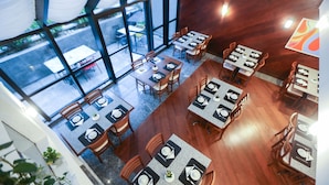 A restaurant with multiple tables and chairs, large windows, and a view of the outside.