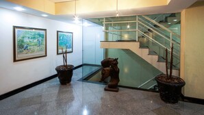 A modern lobby with a glass staircase, framed paintings, and potted plants.