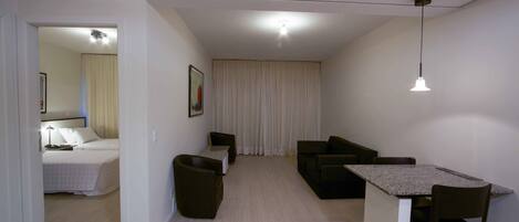Un salón moderno y luminoso con sofá, una mesita y una cama al fondo.