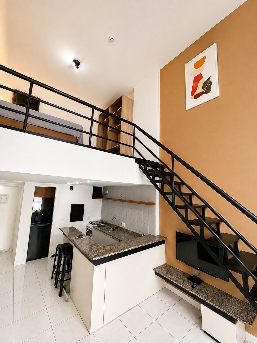 A modern kitchen with a central island, black staircase, and a mezzanine level.