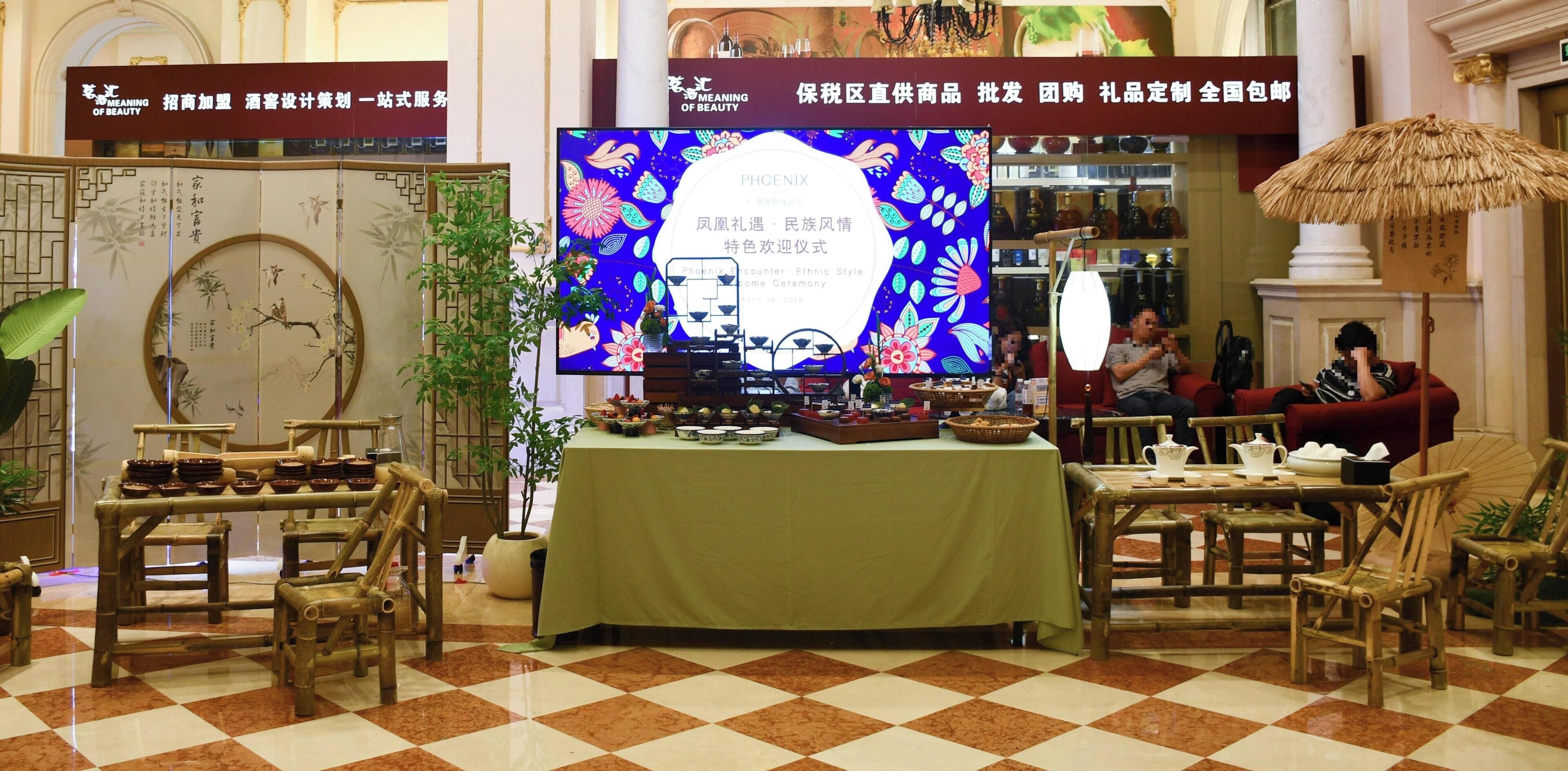 A traditional Chinese tea ceremony setup with a table, chairs, and a large screen displaying a cultural event.
