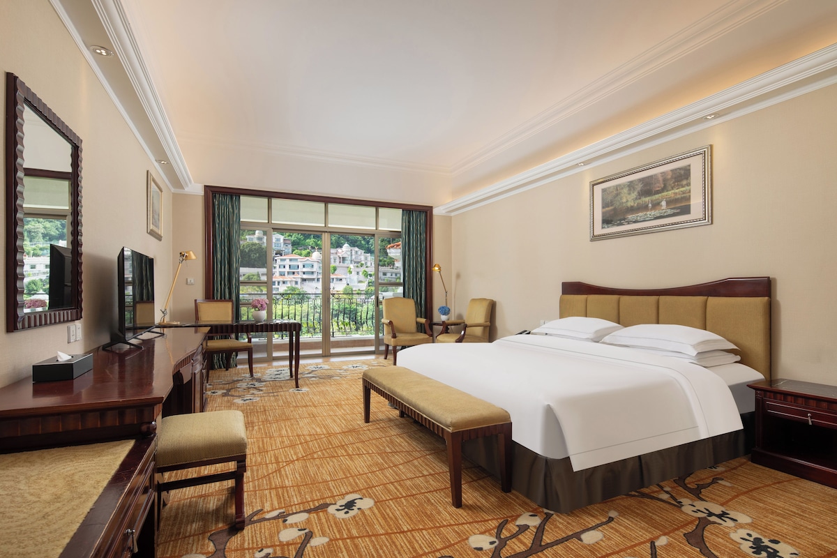 A hotel room with a bed, a desk, a chair, a television, and a view of the outside.