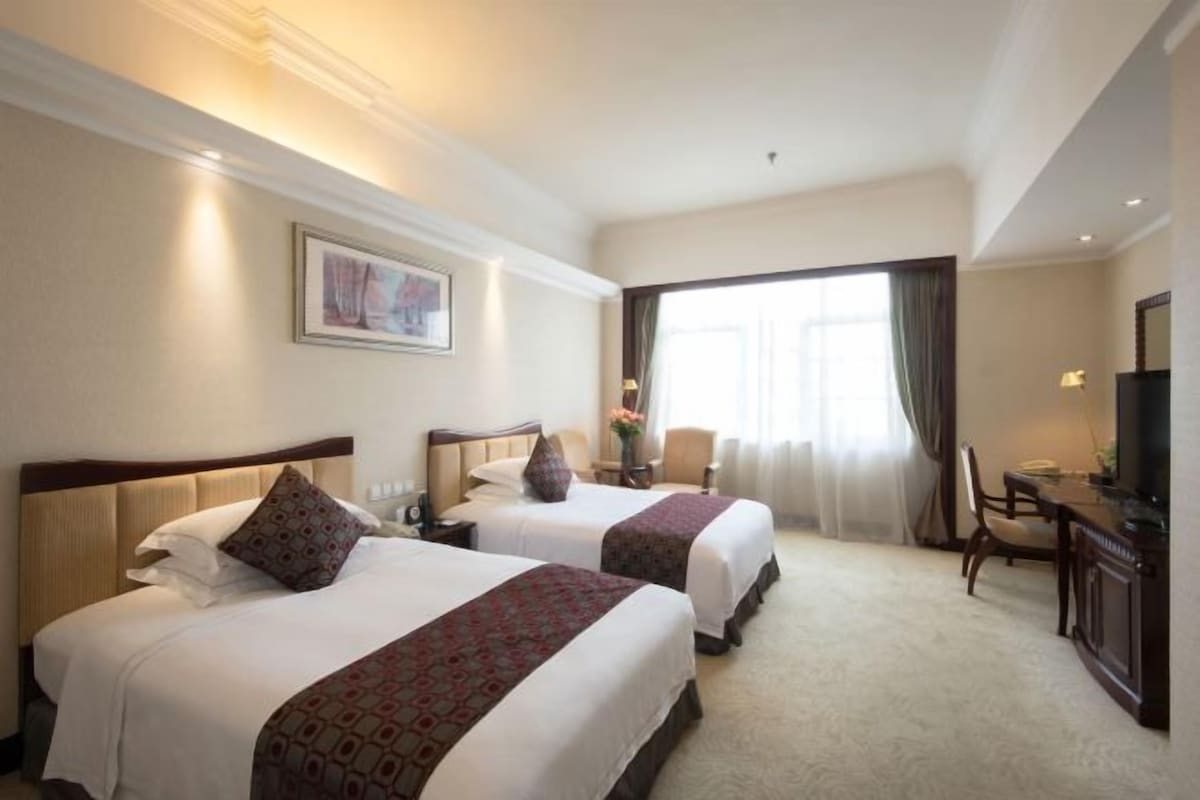 A hotel room with two beds, a desk, a chair, and a television.