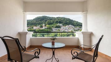 Un balcon avec deux chaises et une table, donnant sur une colline parsemée de bâtiments.