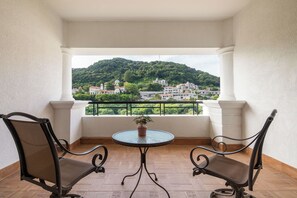 Un balcon avec deux chaises et une table, donnant sur une colline parsemée de bâtiments.