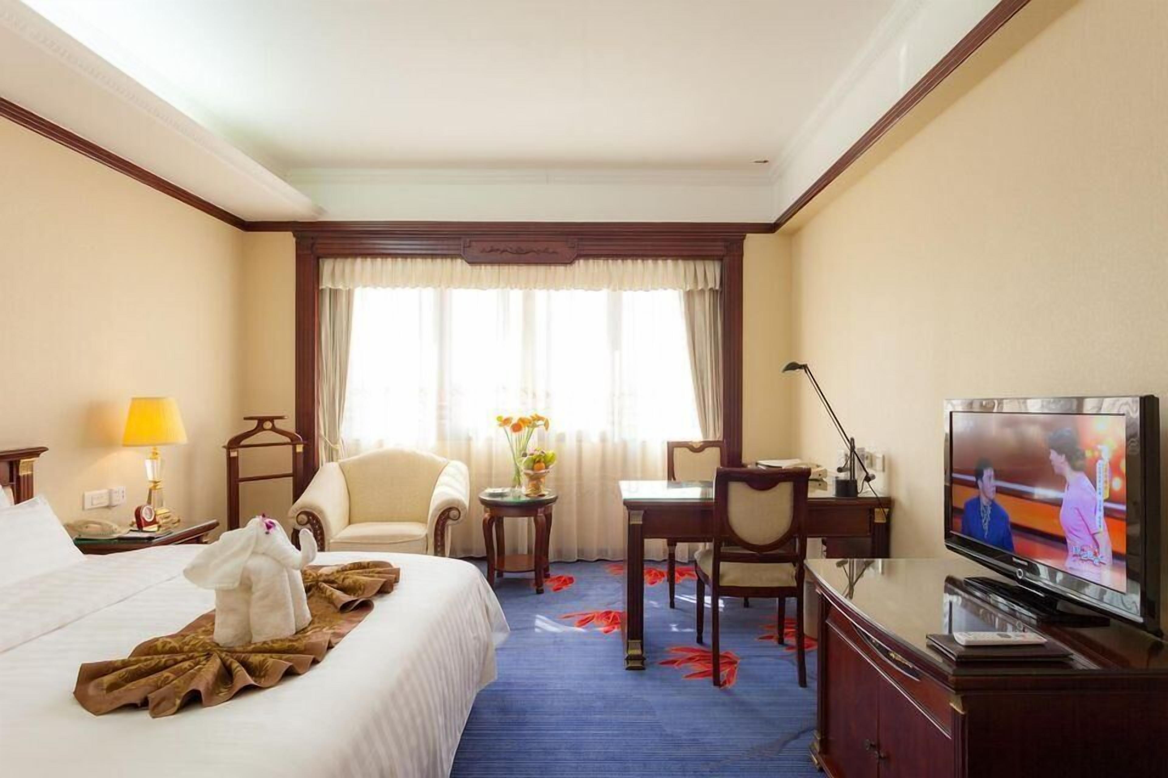 A hotel room with a bed, a desk, a television, and a window with curtains.