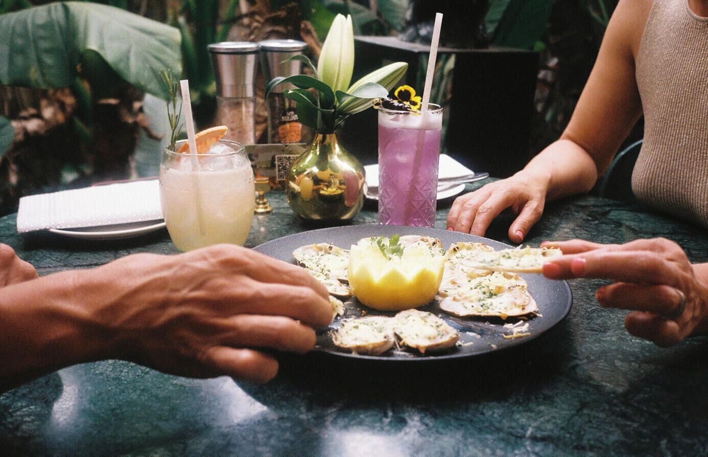 Una mesa con un plato de comida, bebidas y un jarrón decorativo.