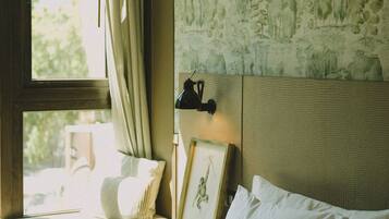 A hotel room with a bed, a nightstand, a lamp, a window with curtains, and a wall with a nature-themed mural.